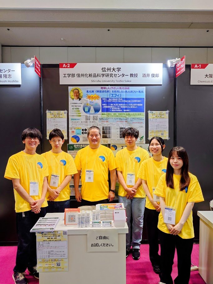 黄色いTシャツを着た酒井教授と学生5名が、エフィのポスターを掲げたブースの前に並んでいる